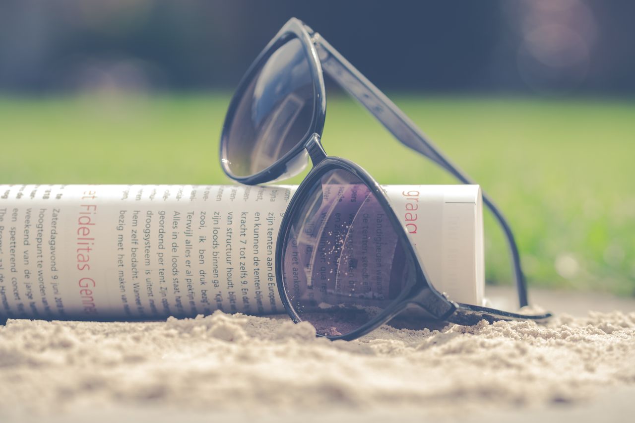 why-choose-us Chic black sunglasses resting with a rolled newspaper in the sand on a sunny summer day.