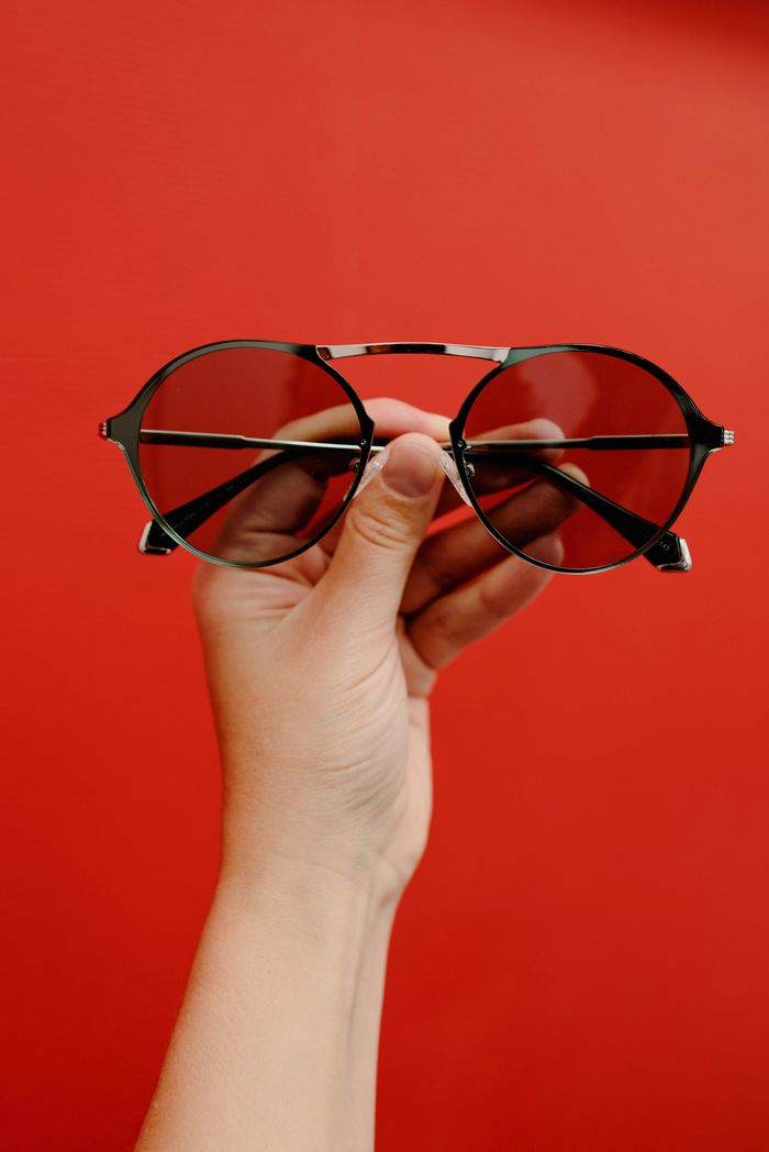 about-bg Crop anonymous person demonstrating stylish sunglasses in metal rim against red background in studio